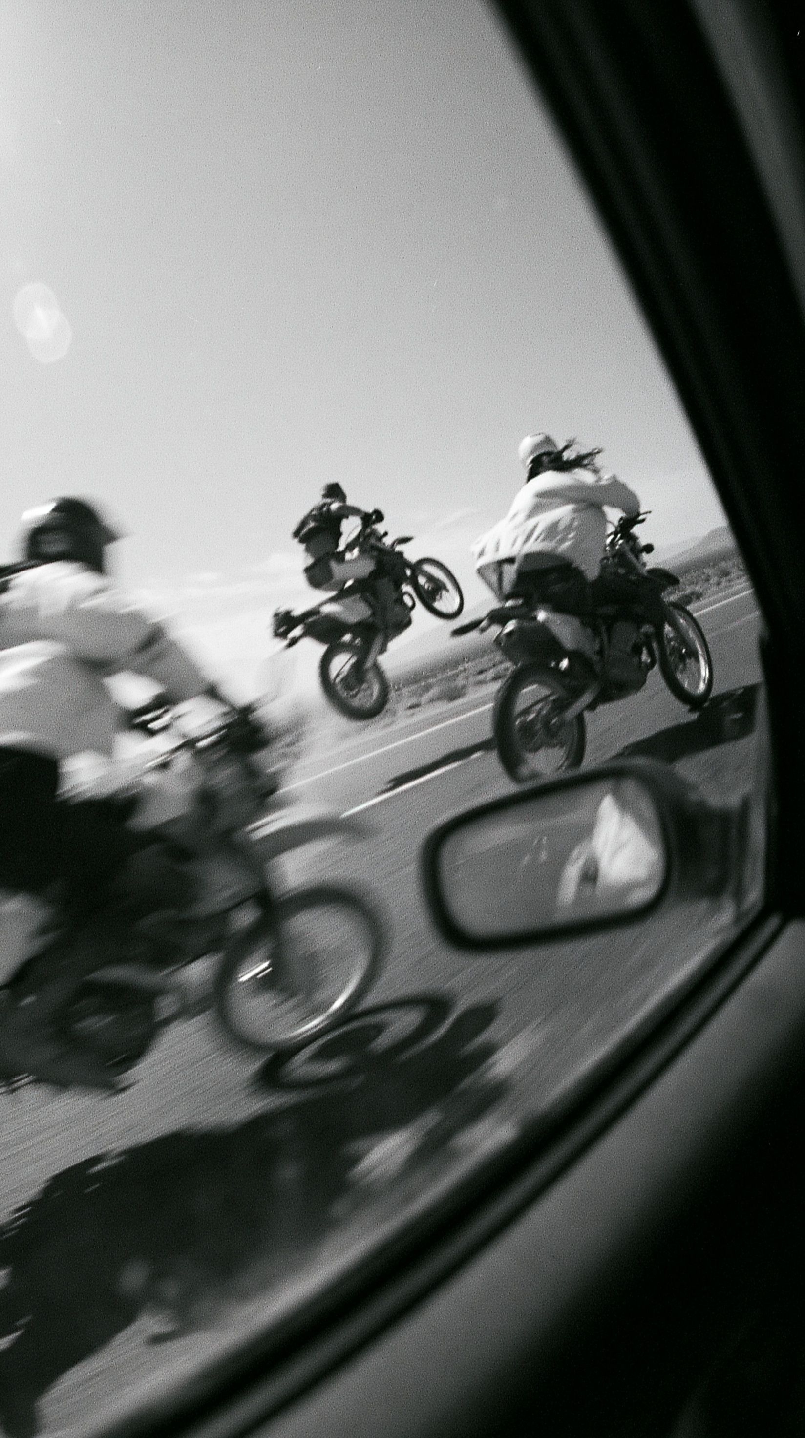 Three motorcycle riders racing past on a desert highway