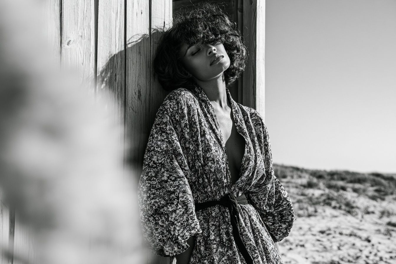 A woman wears an open-style dress on the beach showcasing a natural look