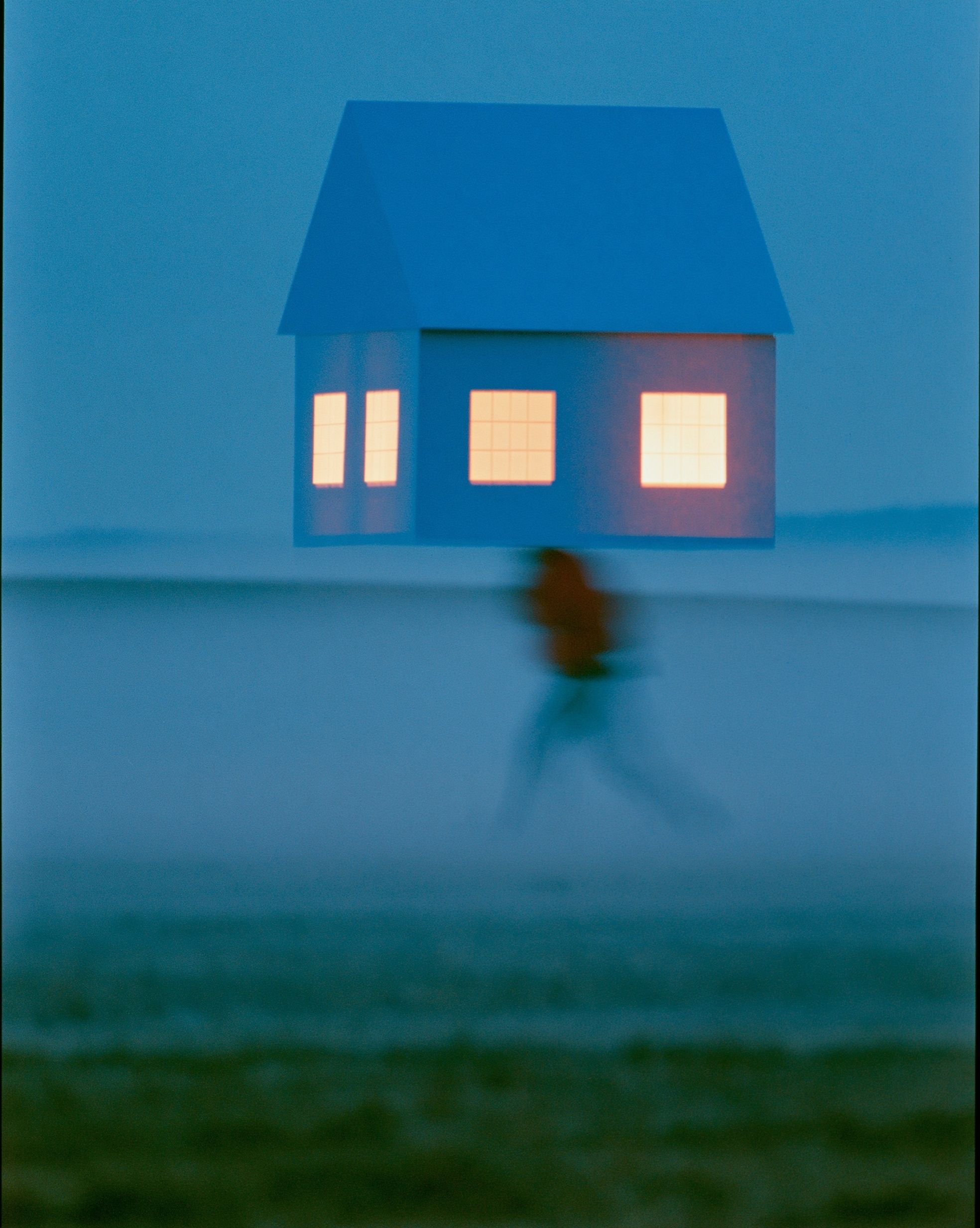 A figure carries a small glowing house across a misty field