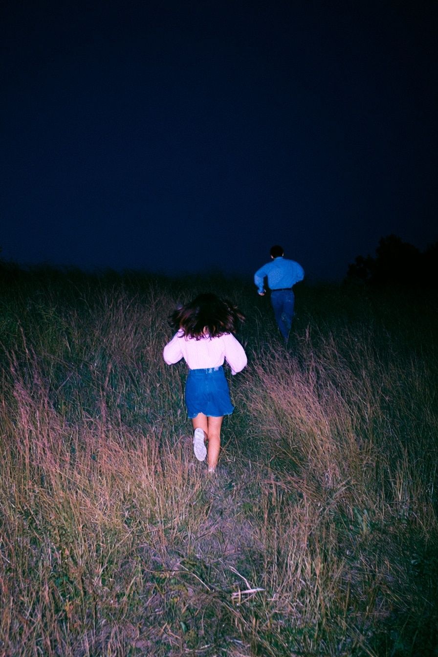 女性と男性が夜に tall grass の田を走っている
