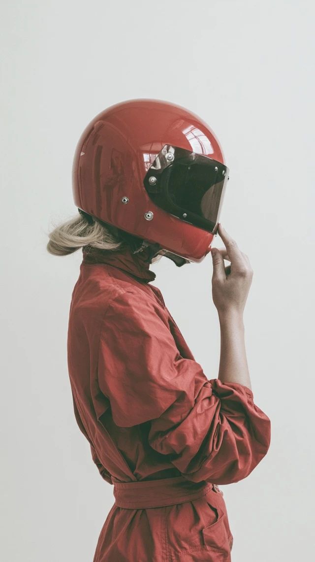 Blonde woman in a red racing jumpsuit shown from behind wearing a vintage racing helmet