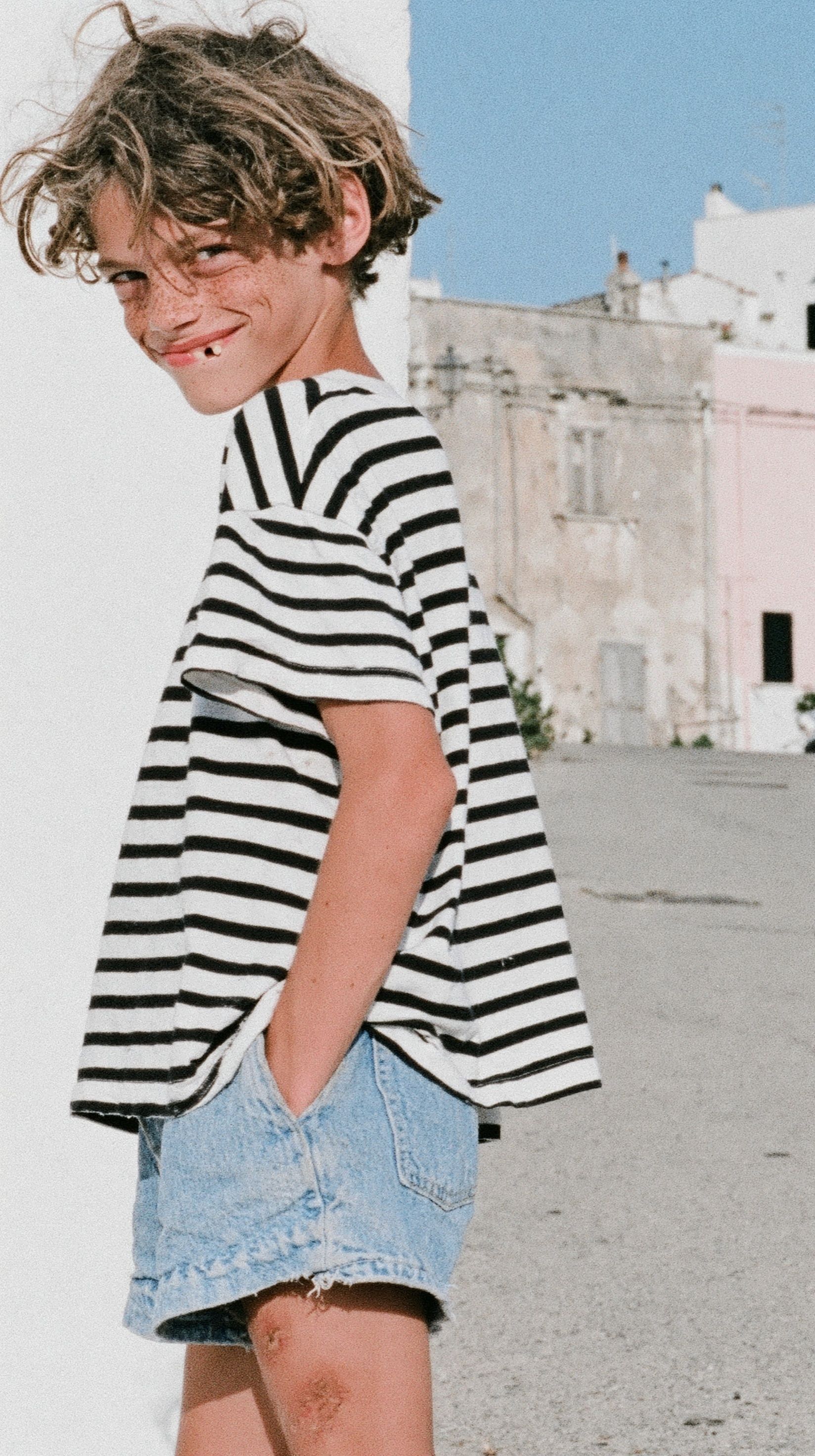 Un garçon européen espiègle portant un T-shirt rayé vintage et un short en jean usé