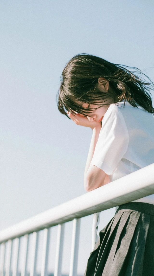 Eine junge asiatische Frau im Schuluniform schützt ihr Gesicht vor dem Wind