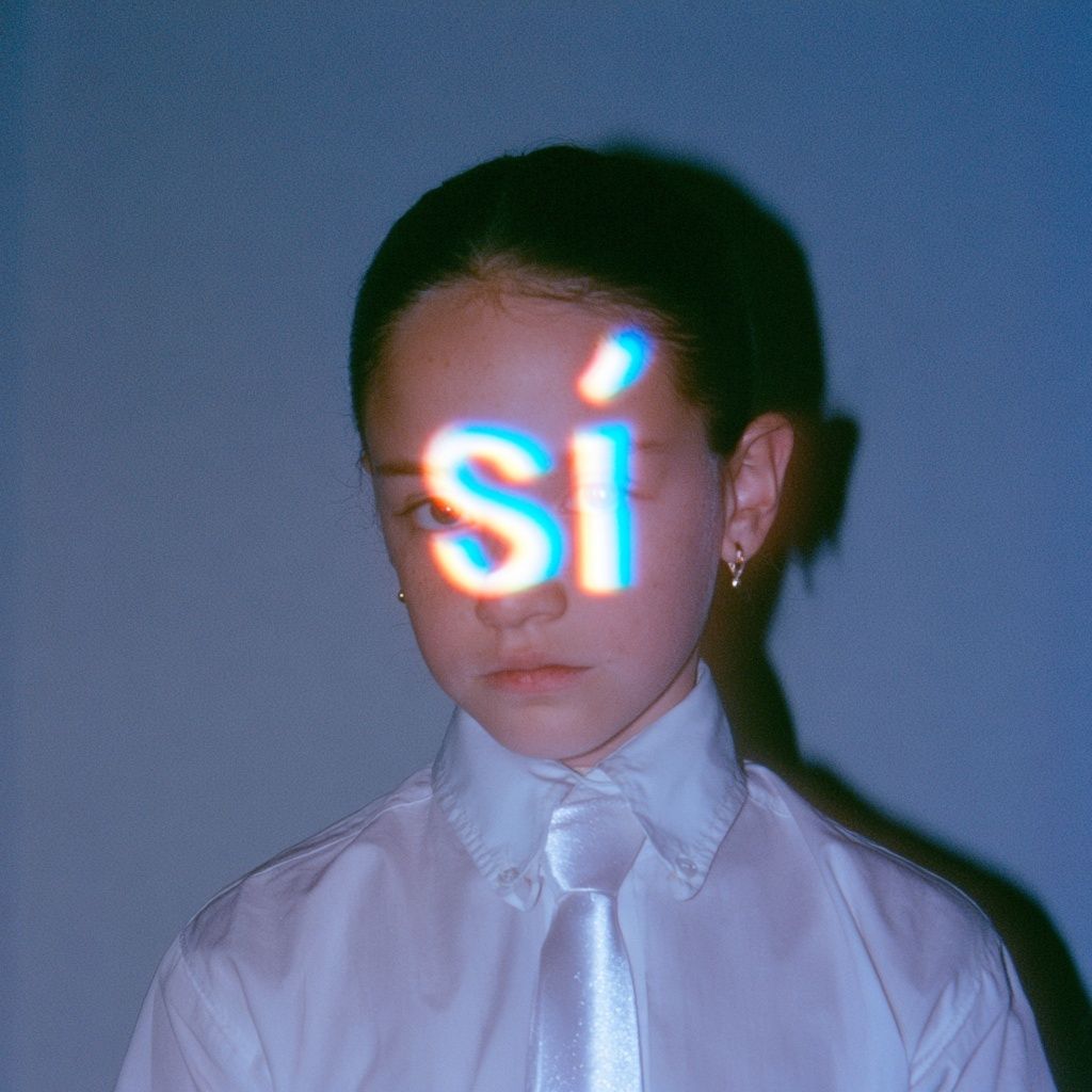 A girl has the word 'sí' projected with light over her face